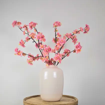 Zijden boeket met roze bloesemtakken in witte vaas