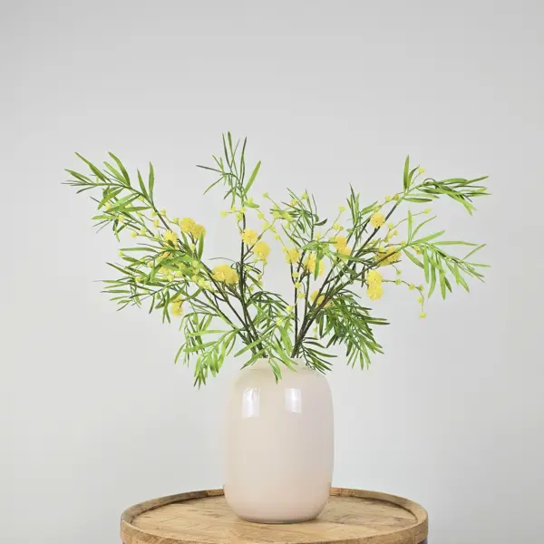 Kunstboeket met groen-gele mimosatakken in witte vaas