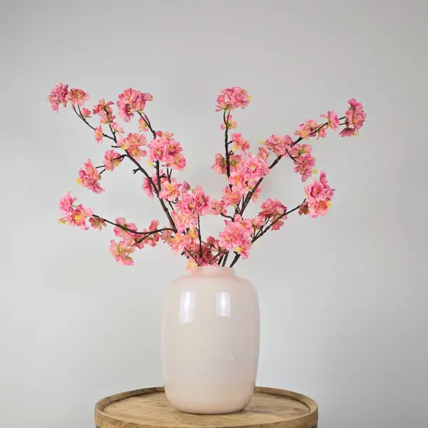 Zijden boeket met roze bloesemtakken in witte vaas